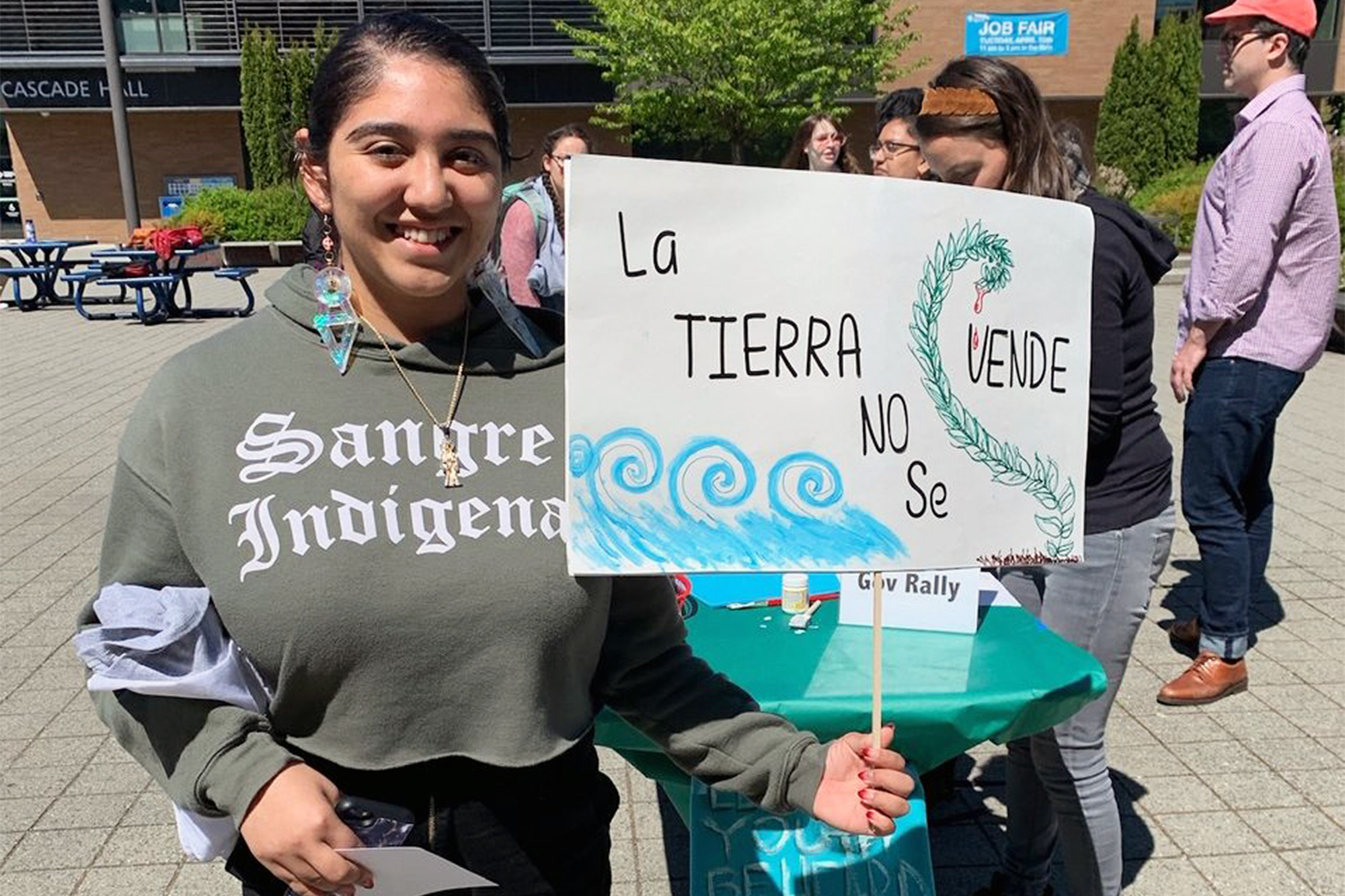 Indigenous student holding a sign that says 'la tierra no se vende' which means 'the land isn't for sale'