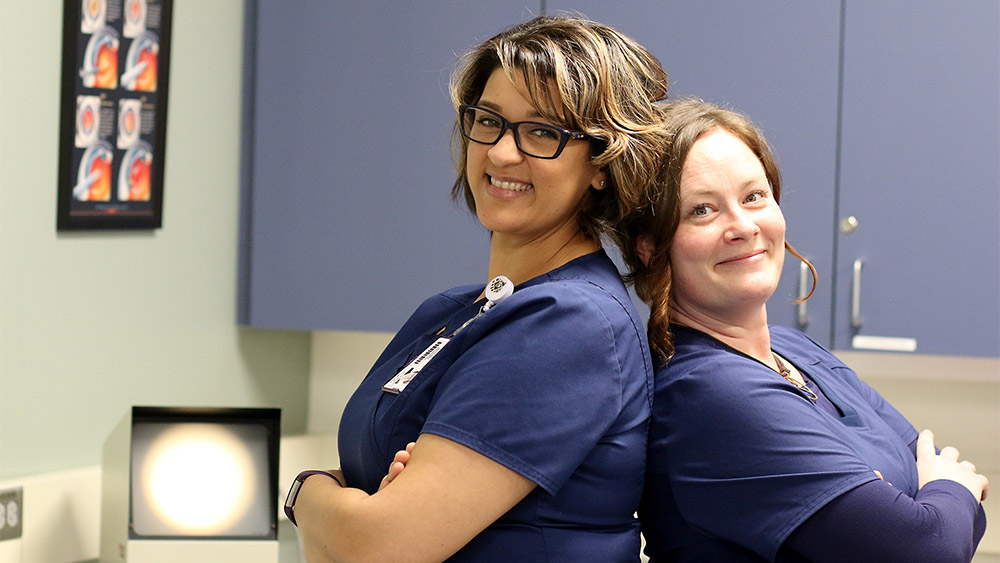 Two students in scrubs standing back-to-back