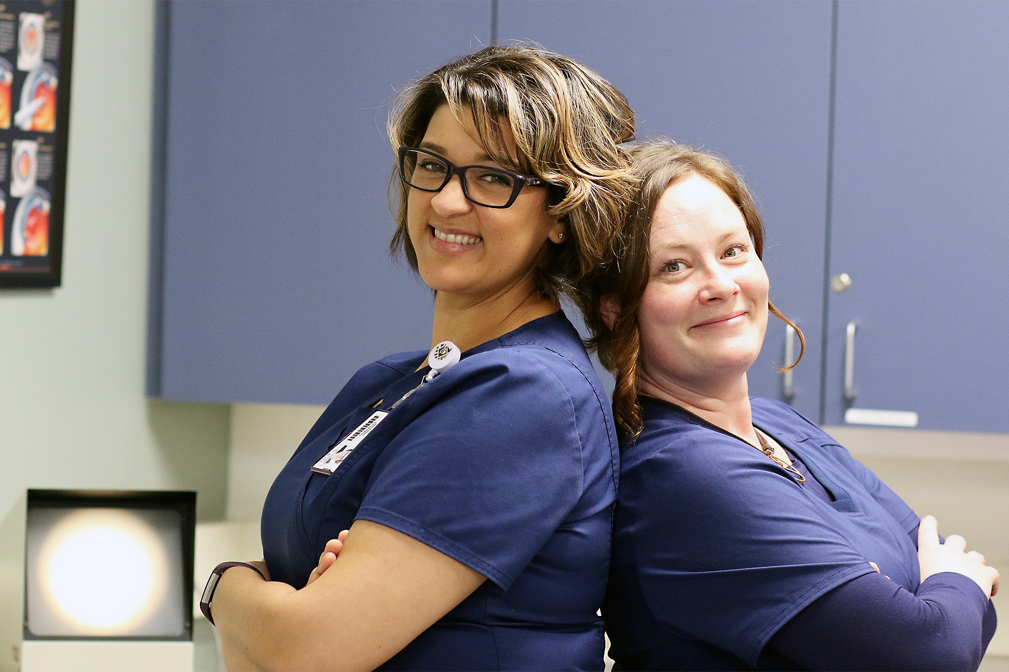 Two Health Information Students students in scrubs standing back-to-back and smiling at the camera