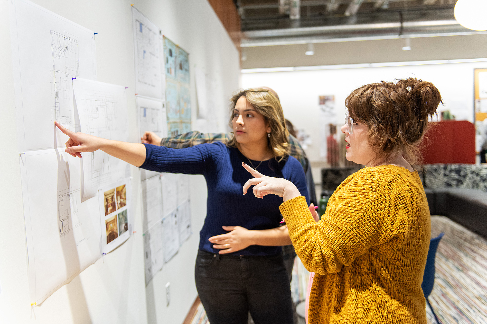 Interior Design students pointing at and discussing plans up on a wall