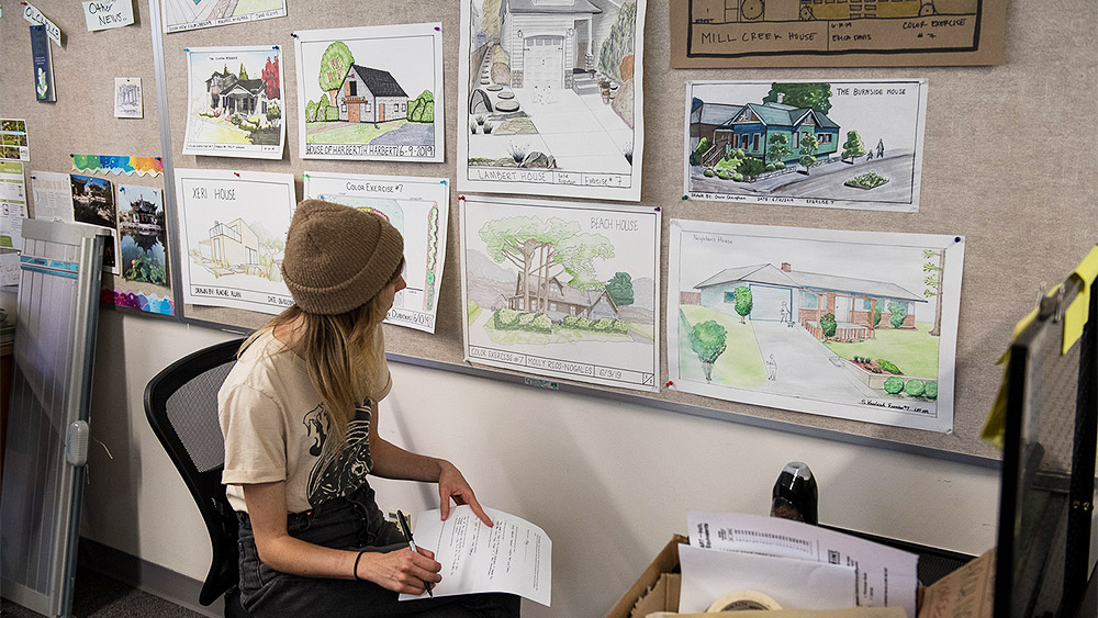 Student taking notes at a board filled with landscape design sketches