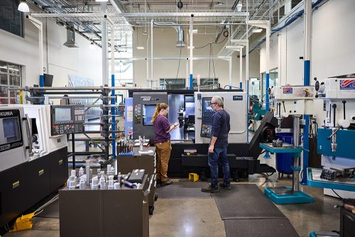 Wide view of the workshop, with a student and her instructor working at a machine