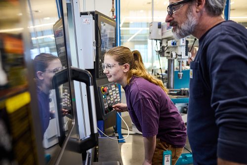Student operating machinery with her instructor watching
