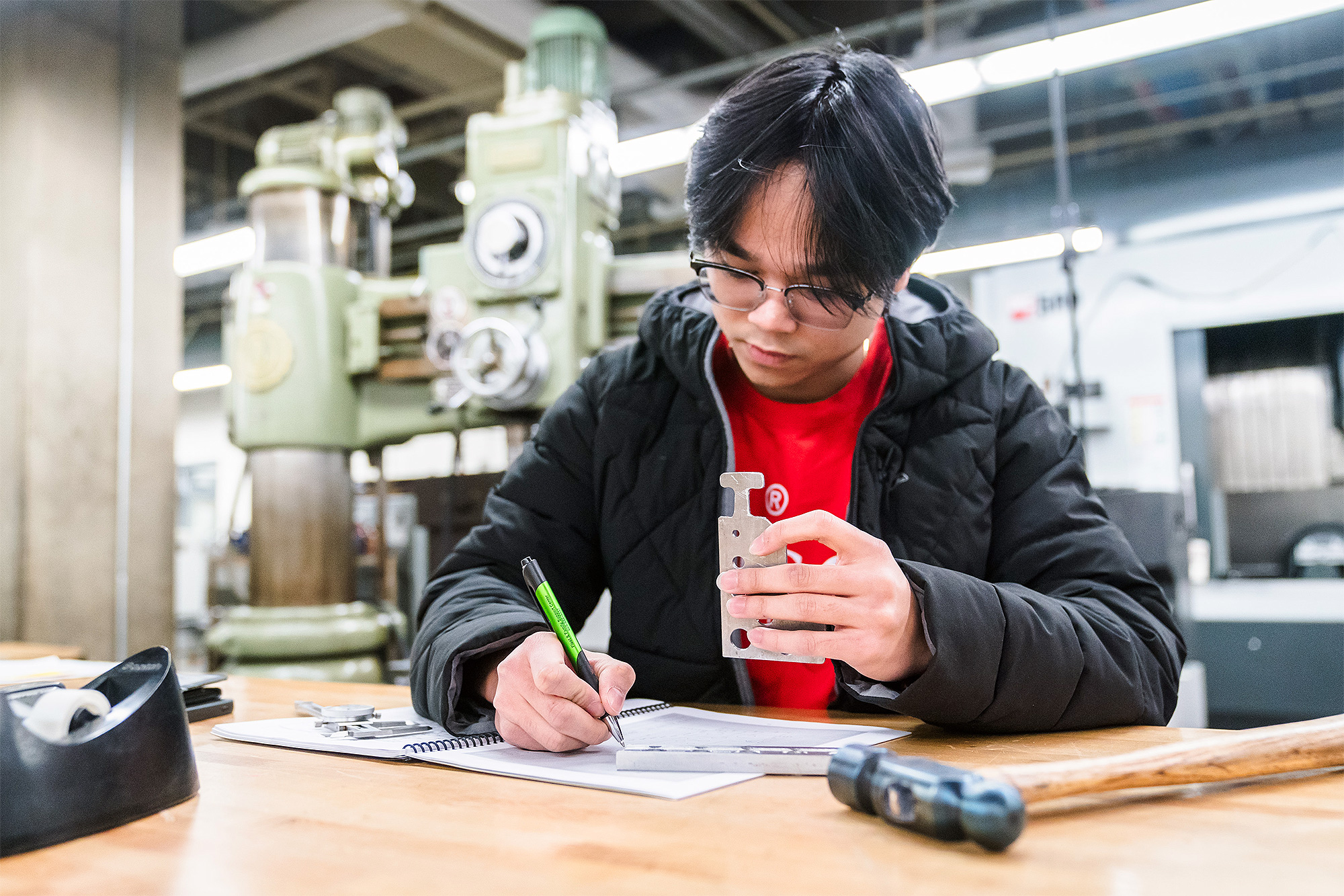 Machine Manufacturing student writing down calculations and holding a machine part