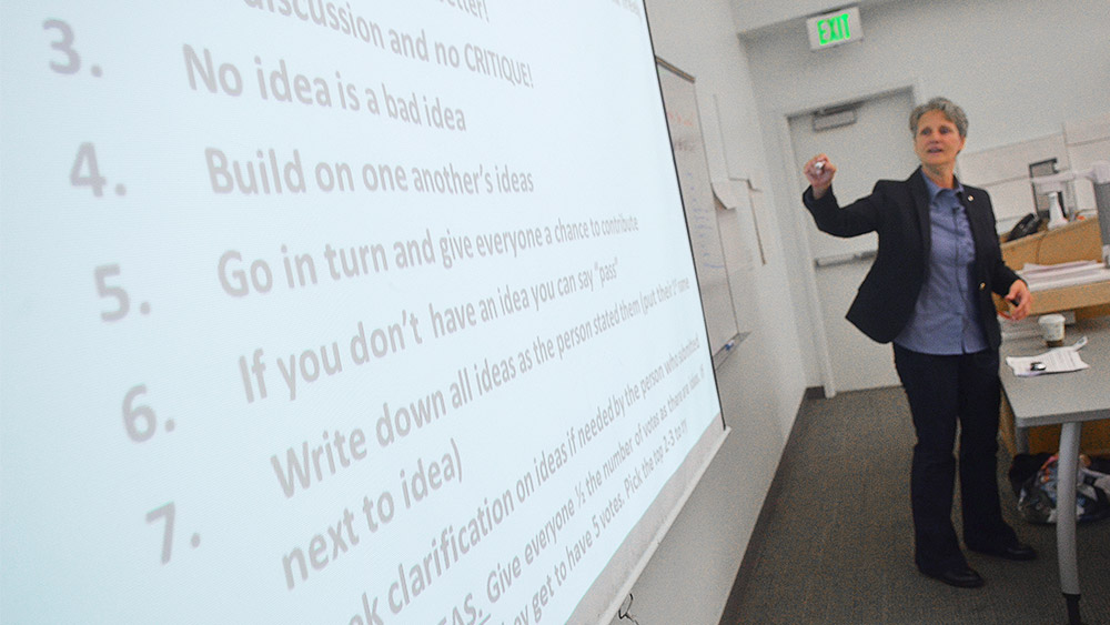 Instructor teaching in front of a whiteboard that says things like 'no idea is a bad idea' and 'build on each other's ideas'