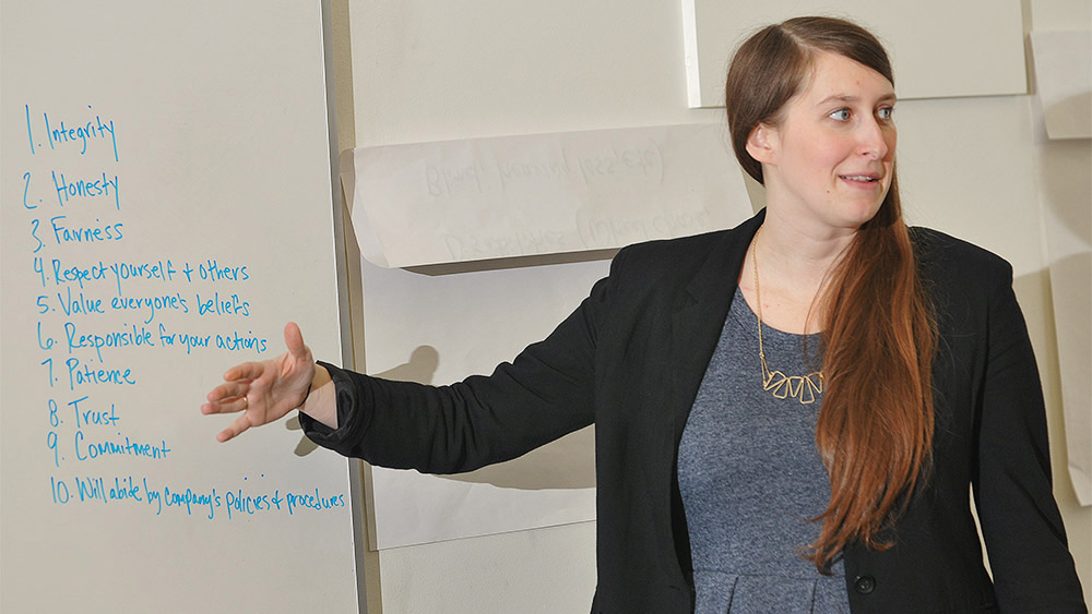 Student presenting to a class in front of a whiteboard with a list of words that describe a good manager