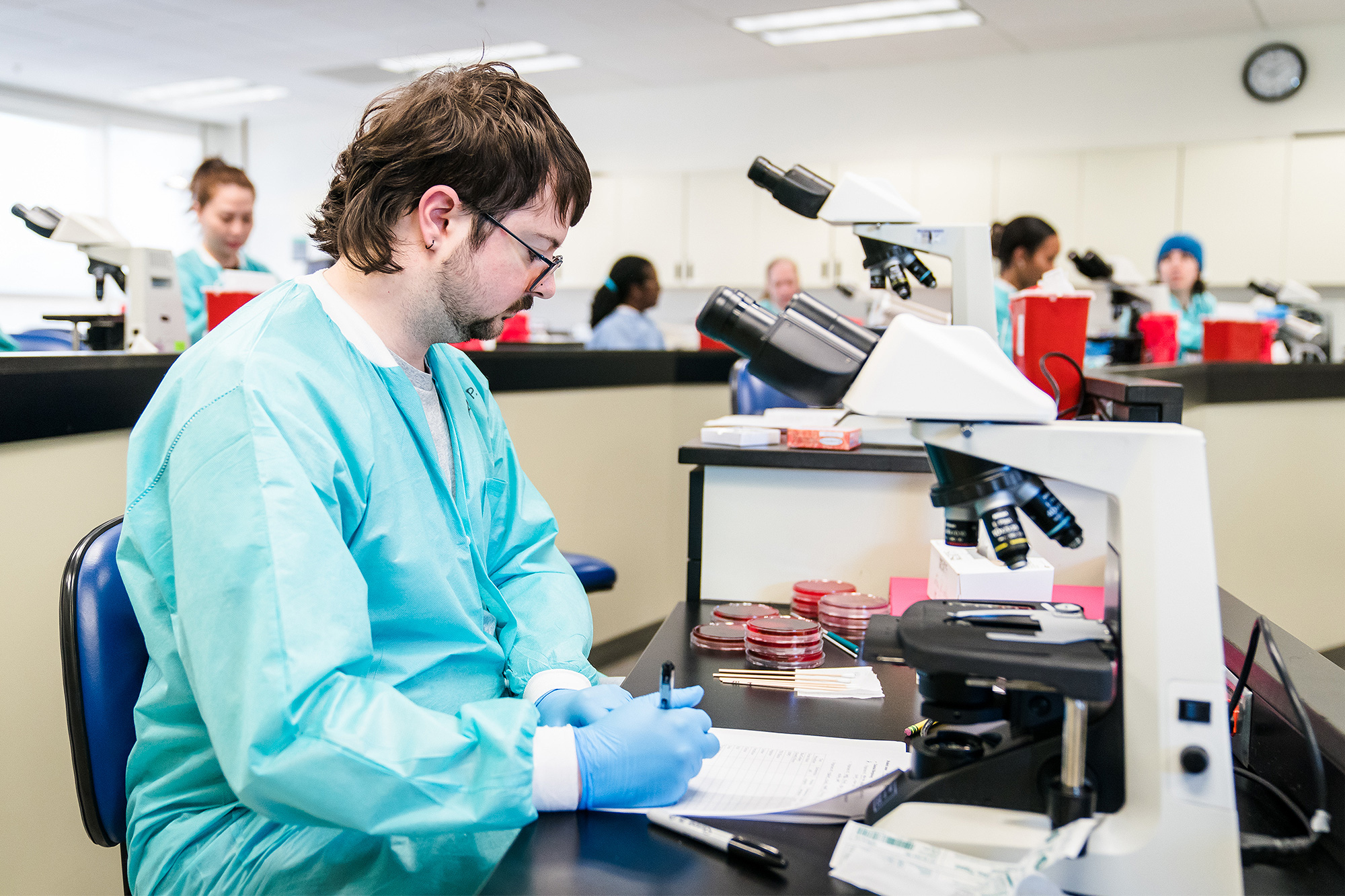 Medical Lab Tech student taking notes at a microscope