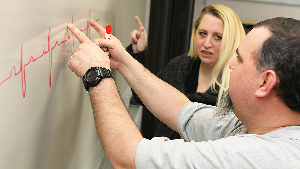 Student and instructor looking at a heartbeat diagram on a whiteboard