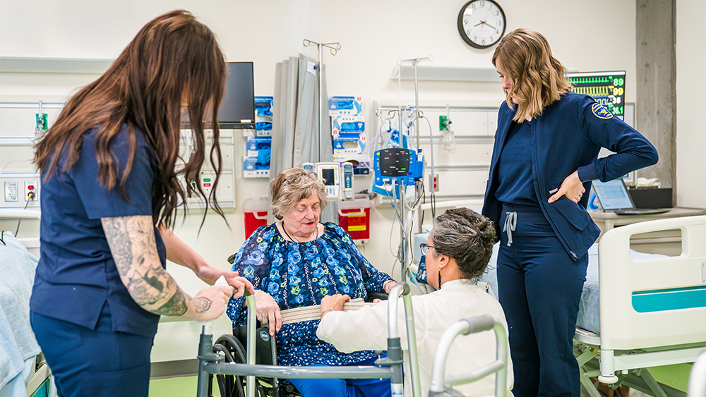 Students learning how to assist an elderly patient in a wheelchair