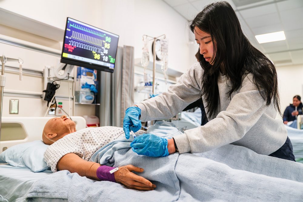 Nursing student checking a mock patient's IV connection