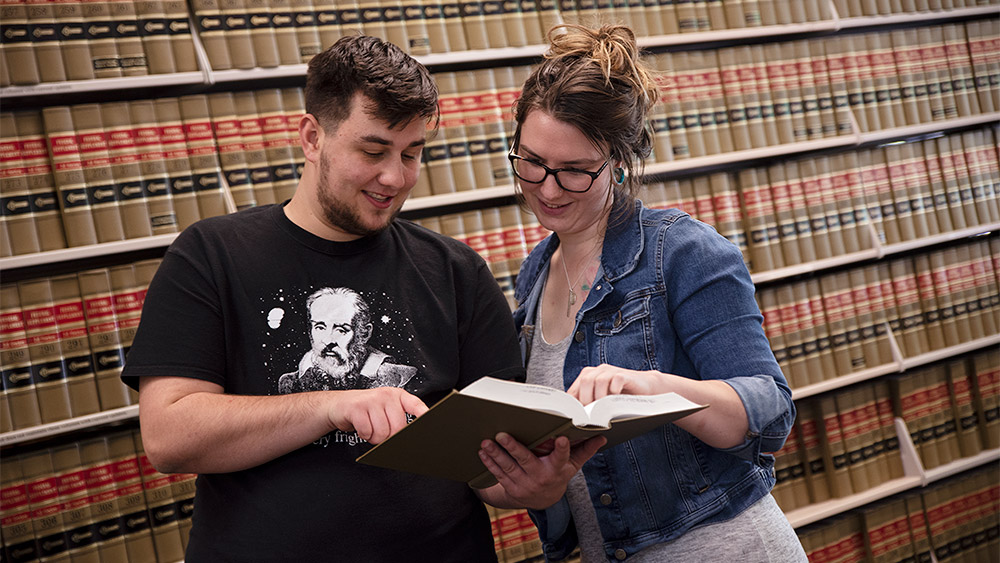 Students looking at a book together in the paralegal library