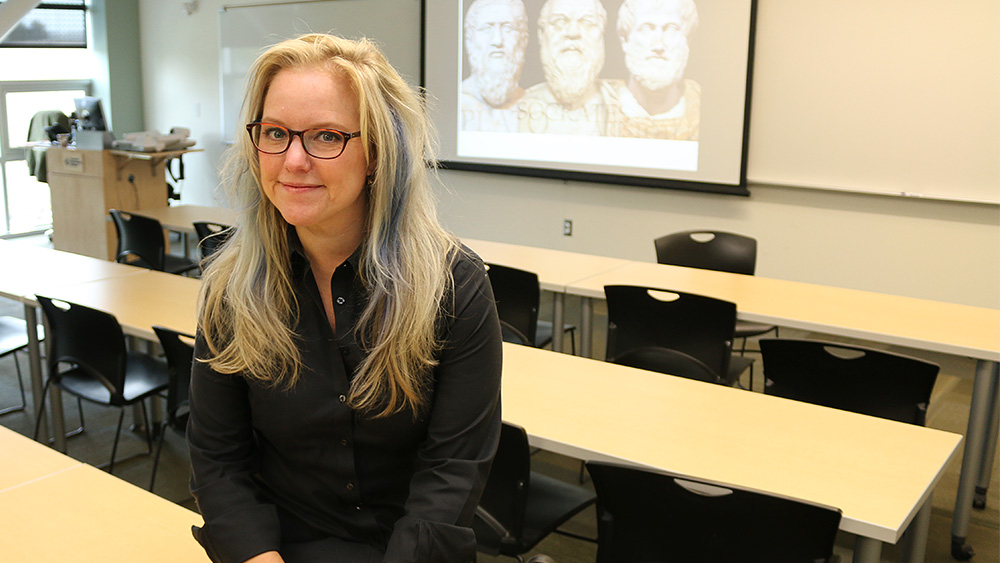 Philosophy instructor in a classroom with an image of famous philosophers projected in the front
