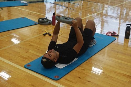 Student laying on his back and lifting a weight
