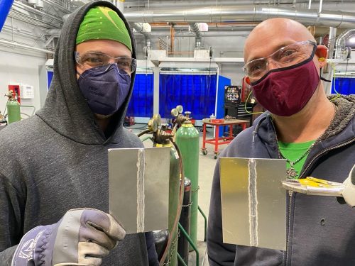 Two students in masks holding their finished welding work