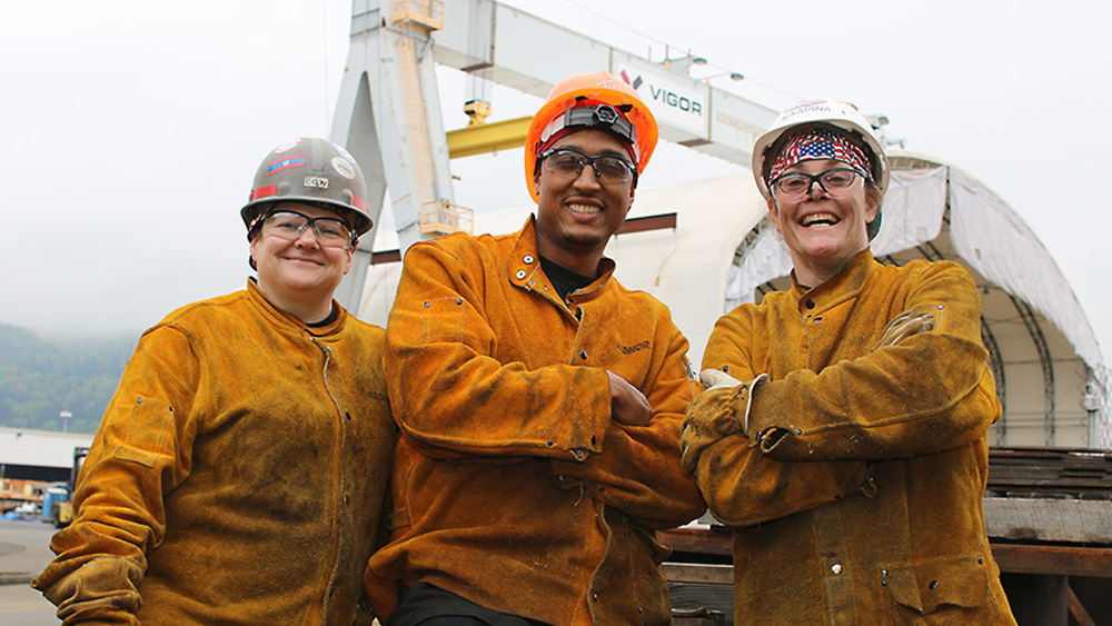 Three welding students standing in a shipyard