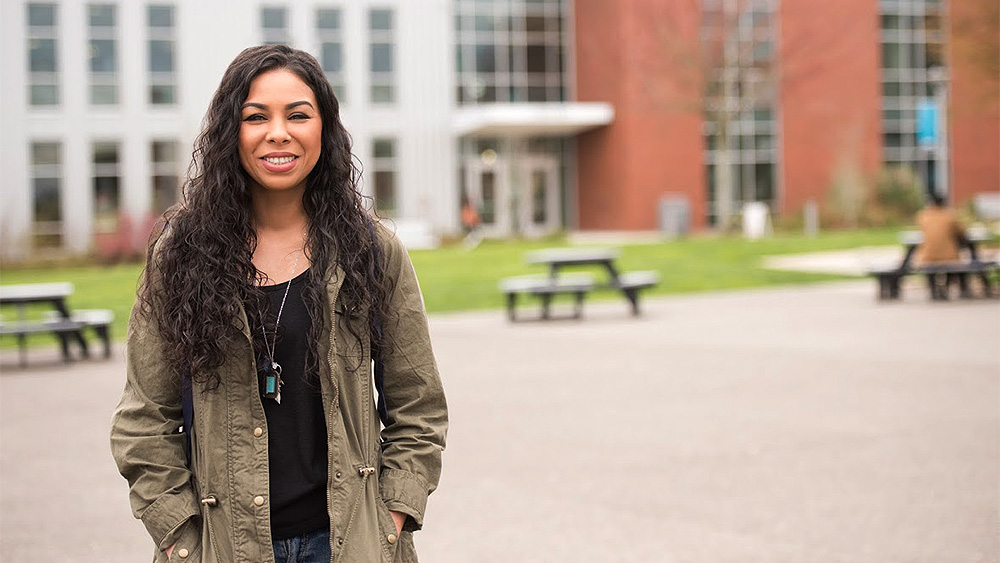 Female-presenting student standing outside looking at the camera