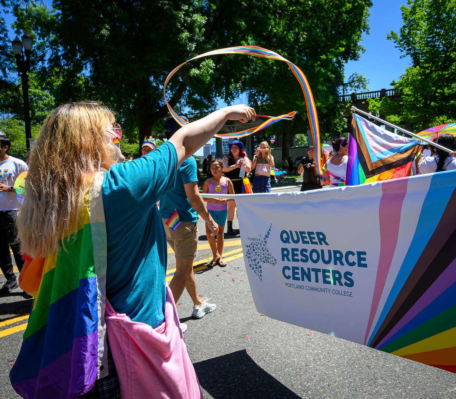 PCC Students in rainbow gears carry a banner that says Queer Resource Centers