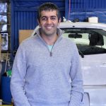 SBDC Client Farhad Ghafarzade standing in front of cars at Green Drop Garage