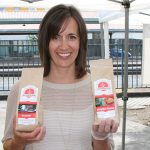 Marilyn Kember, owner at Kember’s Gluten Free, smiles while holding up two bags of her baked goods recipe mixes, one in each hand
