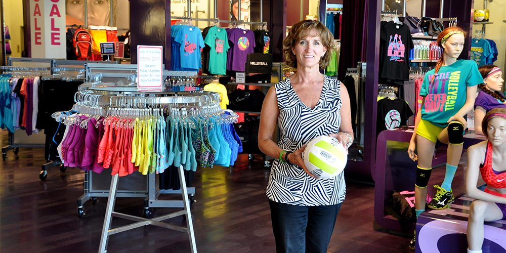 Owner of Aries Apparel athletic wear standing holding volleyball in retail store