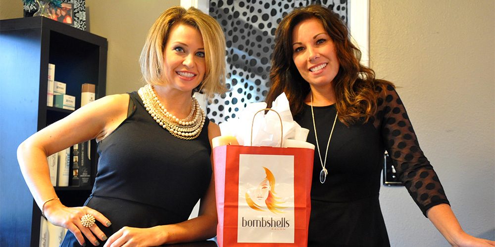 Bombshellers business women smiling with a gift bag of their product