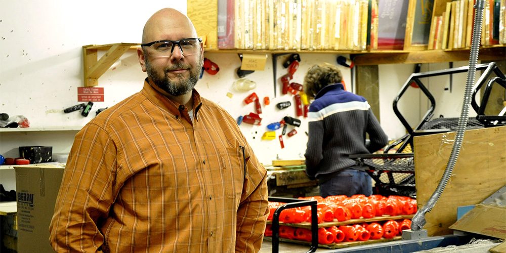 Protoco Enterprises employee in orange shirt stands in business workshop.