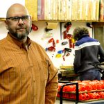 Protoco Enterprises employee in orange shirt stands in business workshop.