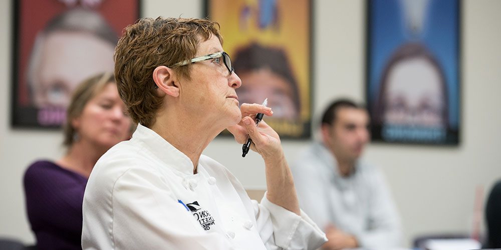 Woman in white chef uniform sitting in PCC CLIMB classroom