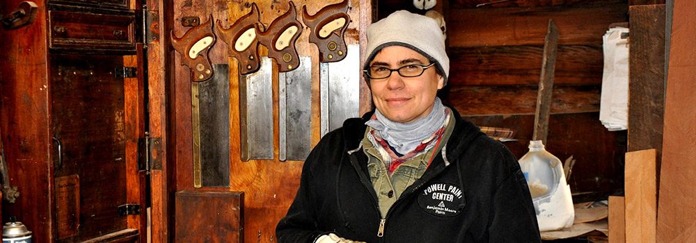 Amy McAuley, owner of Oculus Fine Carpentry in front of saws in wood shop