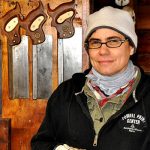Amy McAuley, owner of Oculus Fine Carpentry in front of saws in wood shop