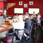 Interior of busy restaurant with red walls and man behind bar.