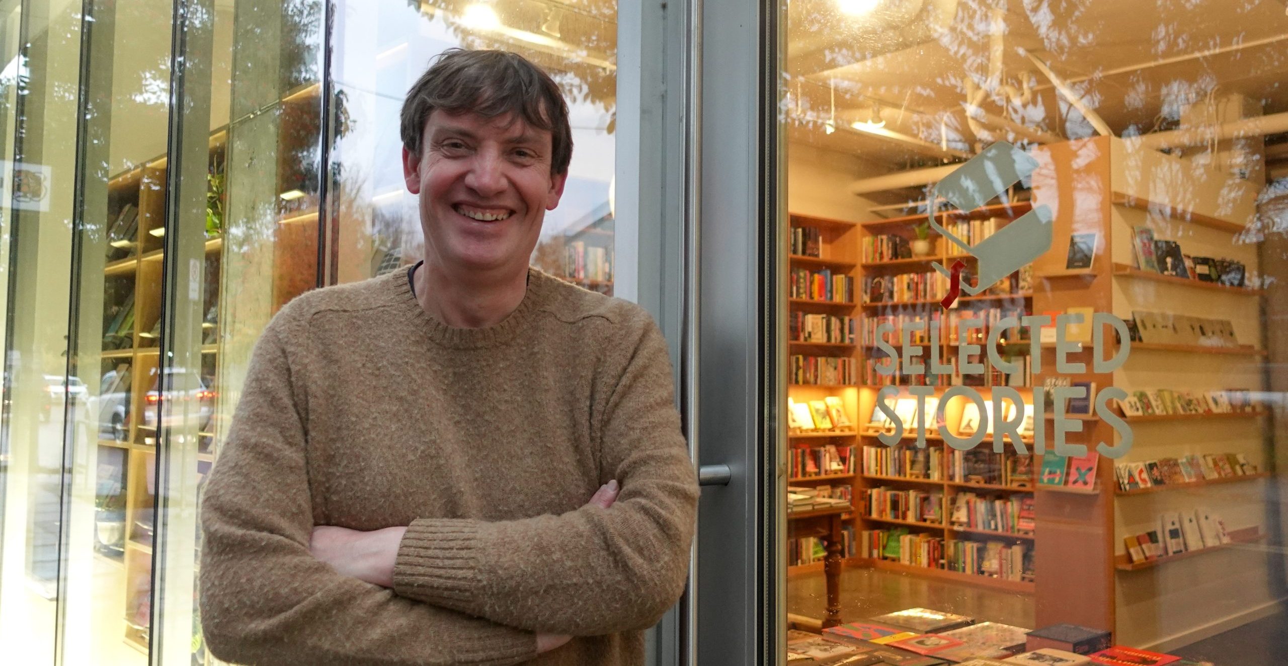 Christopher stands in front of his bookshop entrance