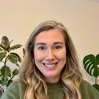 Person with long blonde wavy hair, light skin tone, smiling, and wearing a green sweatshirt.