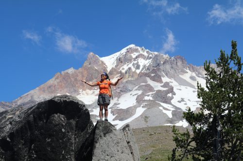 Faith atop a large bolder. Behind her is Mt Hood. The skies are blue with a few clouds.
