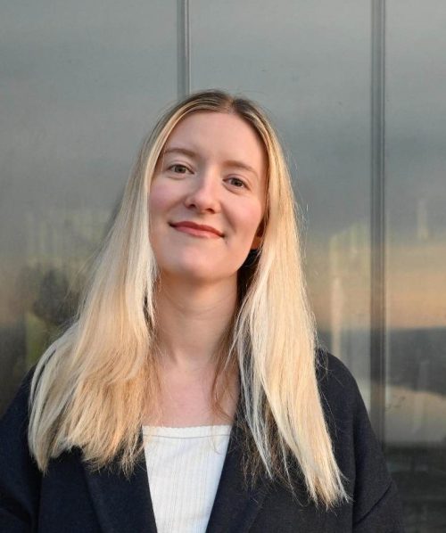 Greta, wearing a long blue coat and staring straight at the camera