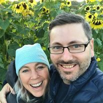Janis and her partner Justin smiling in front of a sunflower garden