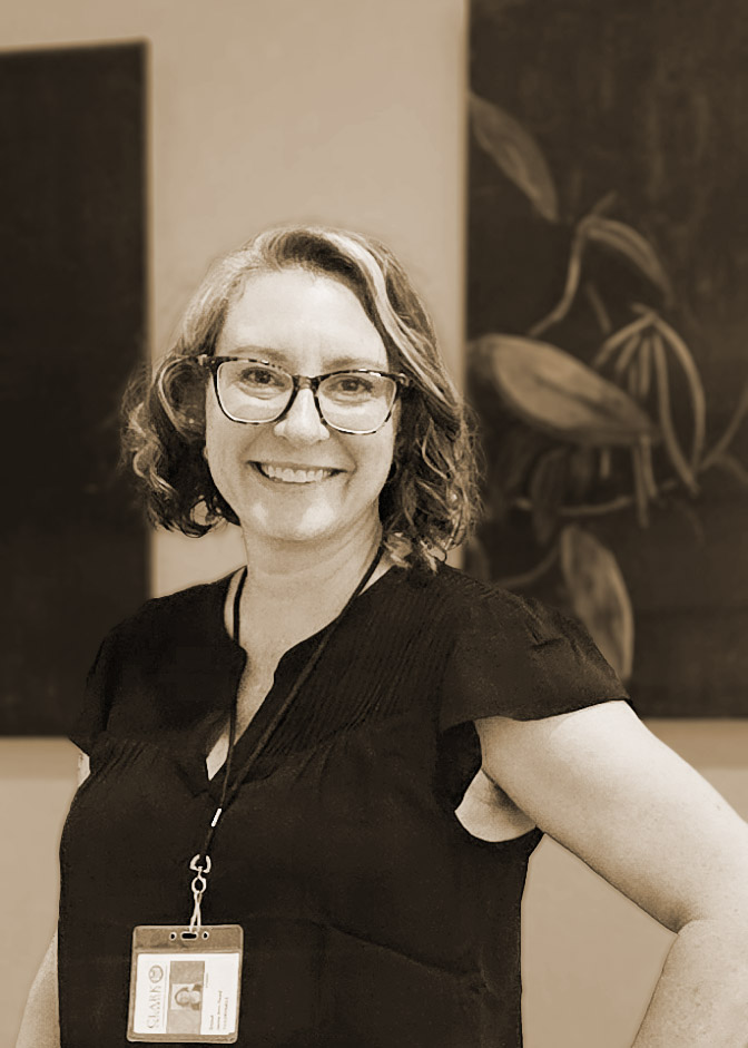 A monotone photograph of a smiling middle aged woman wearing glasses.