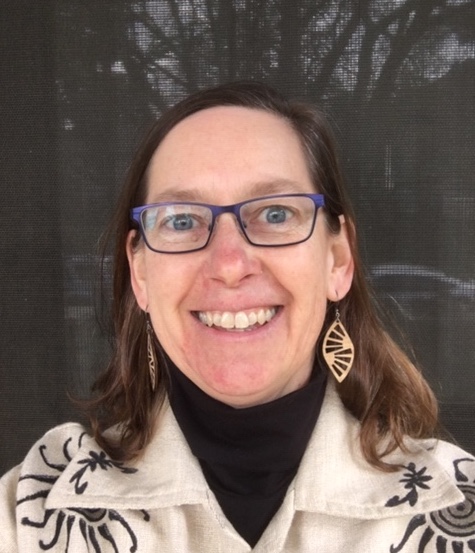 Photo of Julie (woman with fare skin and brown hair wearing blue glasses, light brown earrings, a black turtleneck, and a decorated beige jacket)