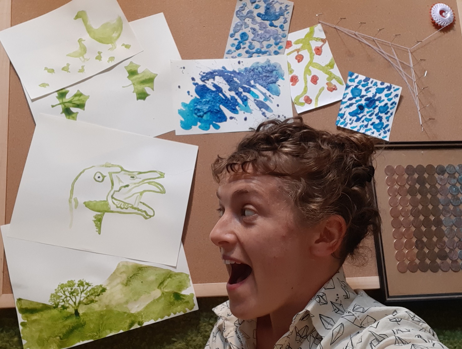 Your course instructor, a white woman in her 30s with curly hair wearing a shirt with an origami print, is in front of a collection of pieces of artworks including a painting of a goose, whose expression she is imitating.
