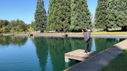 An angler stands on a concrete pad and initiates the cast of a fly rod at an artificial casting pond.