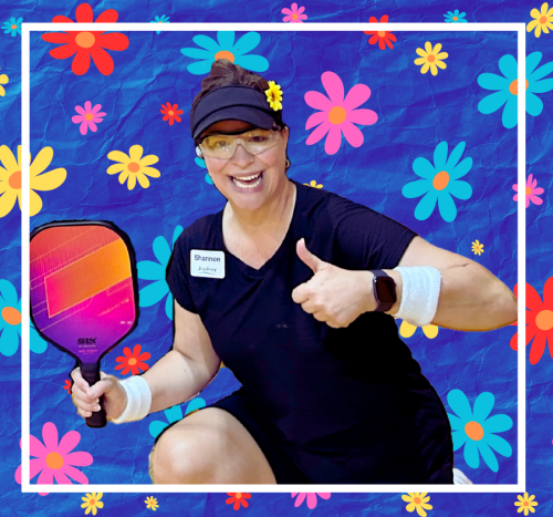 Instructor, Shannon Paul, M.Ed., with a pickleball paddle in hand shows a thumbs up and is in front of a daisy flower background and wearing a daisy flower on her black visor.