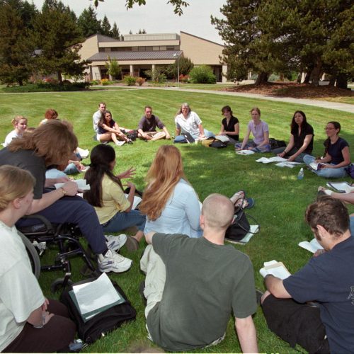 group of students sitting in a circle on campus lawn