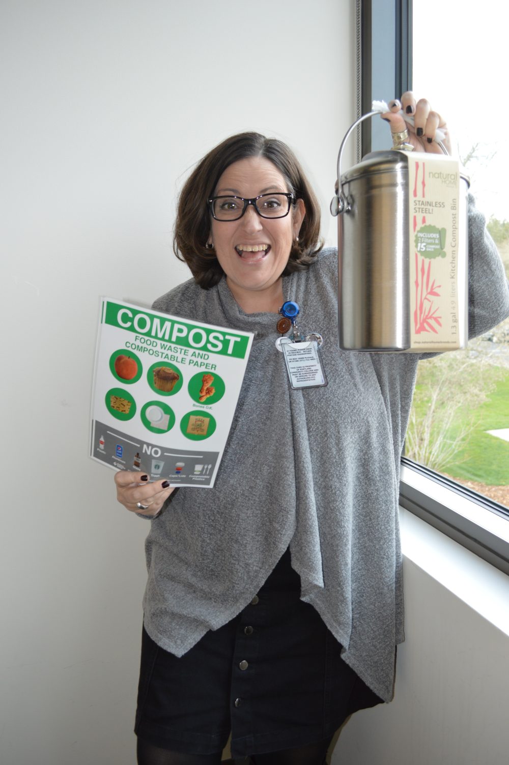 smiling woman raises compost bin and compost instructions poster
