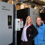 A woman and man pose in front of a boiler.