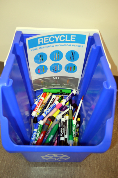 Recycling bucket full of markers and pens.