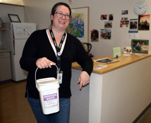 Woan smiles while holding a Universal Waste bucket.