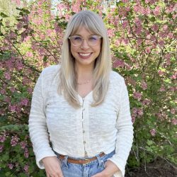 blonde woman standing in front of flower bush