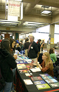 students talk to university staff at tables with paper handouts