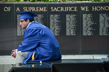 student in PCC cap and gown in front of memorial