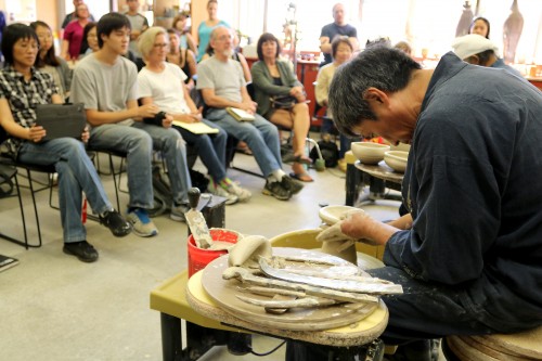 Master potter Kazunao Azuma works the wheel-thrower for the gathered students.